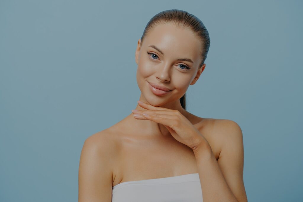 Cosmetic procedures. Pleased woman touching healthy moisturized facial skin after beauty treatment