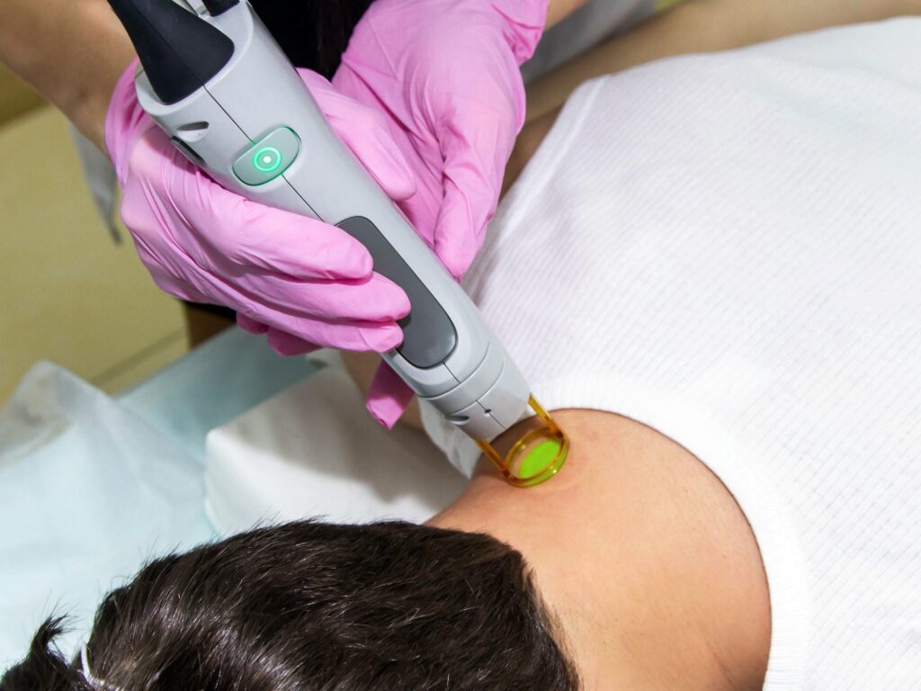 The doctor in pink gloves carries out a procedure of laser hair removal of the neck of a young man